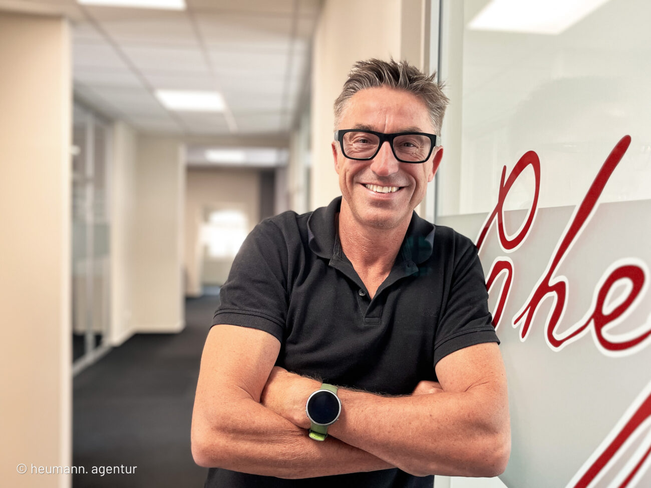 Mann (E. Ulrich Heumann) lehnt an einer Glastür und lächelt freundlich.