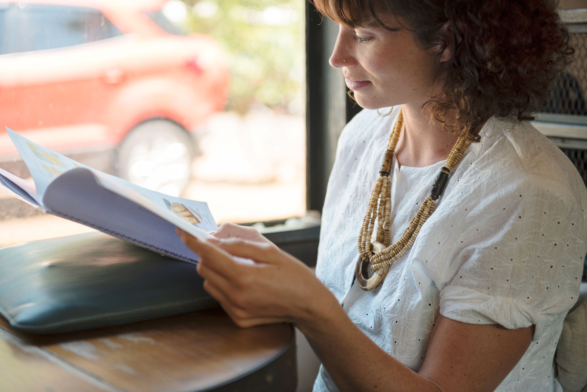 Kundenbindung als Marketingziel 1 Junge Frau sitzt am Fenster und liest ein Magazin